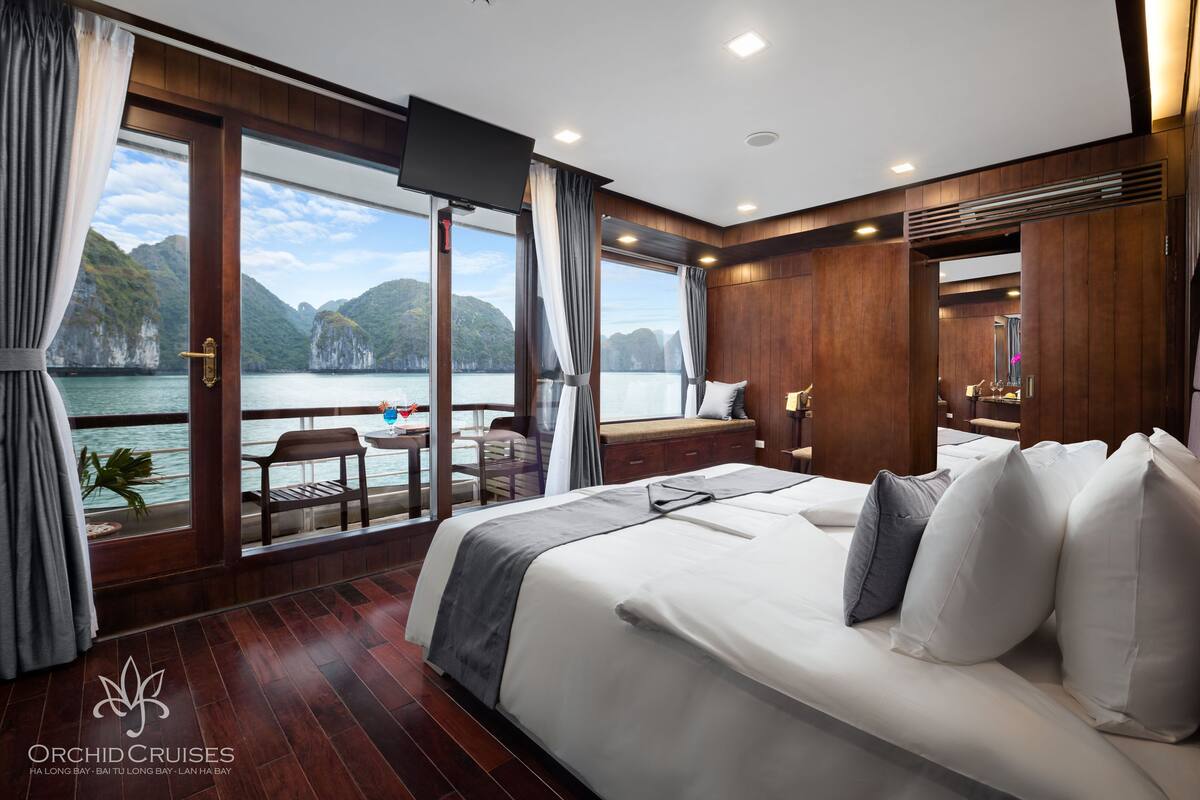 Een ruime slaapkamer met een groot bed, een balkon met uitzicht op zee en een aan de muur bevestigde televisie.