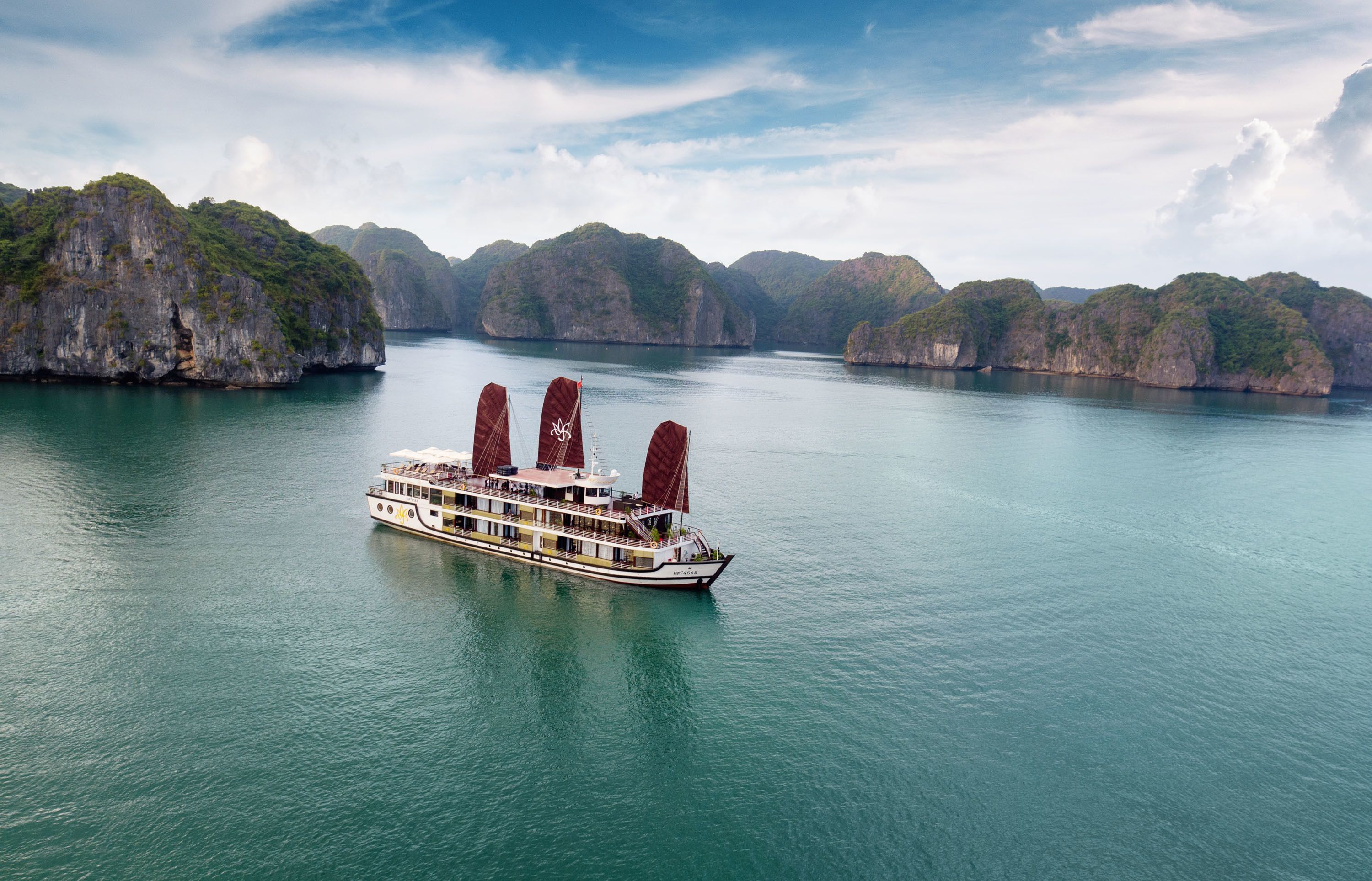 Un bateau de croisière fluviale doté de plusieurs ponts et d’une grande voile, naviguant au milieu de falaises calcaires.