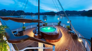 A cruise ship deck with a hot tub, seating areas, and a view of the water and mountains.