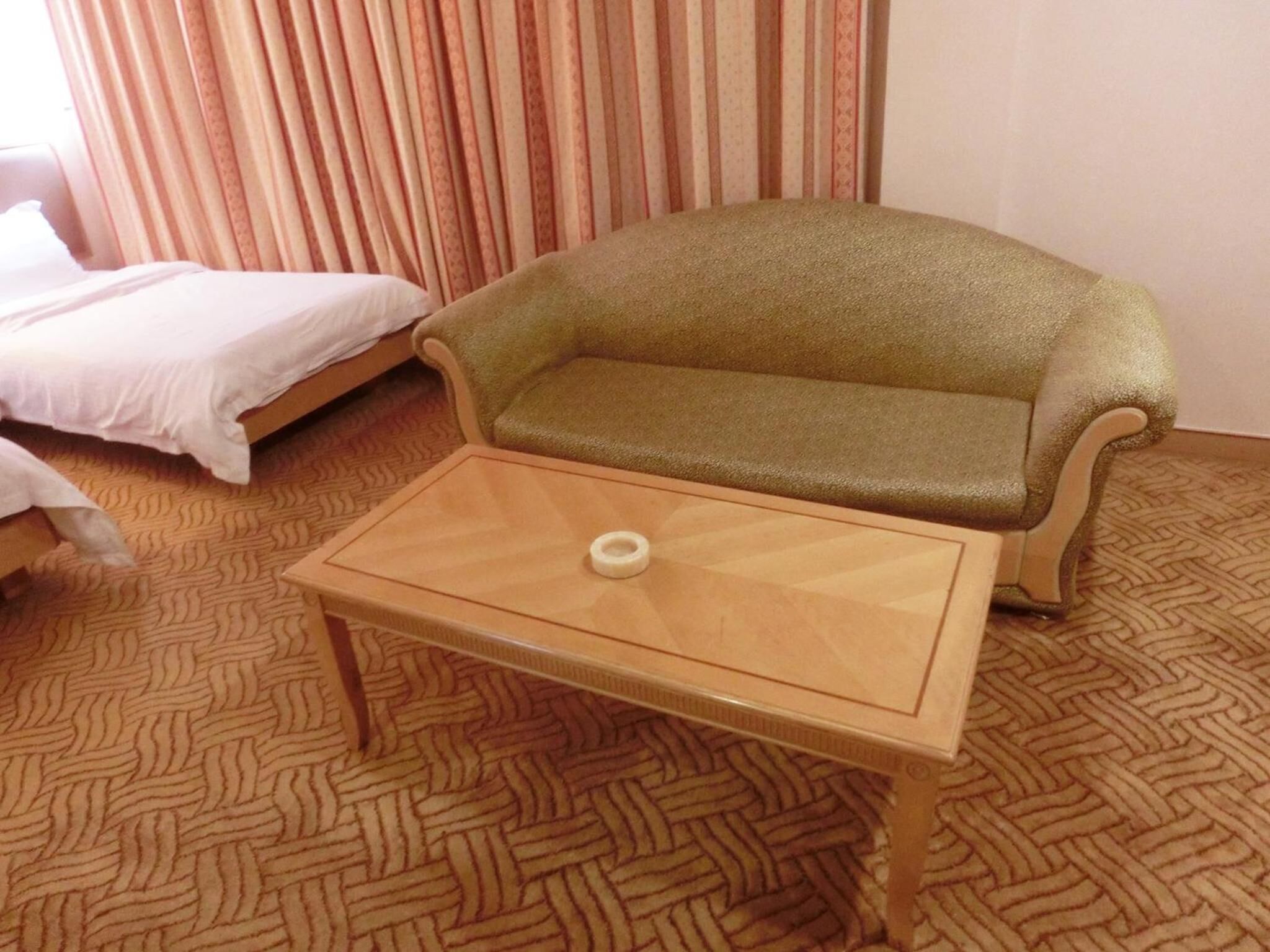 Una habitación con una cama, un sofá verde y una mesa de madera con un objeto blanco encima.