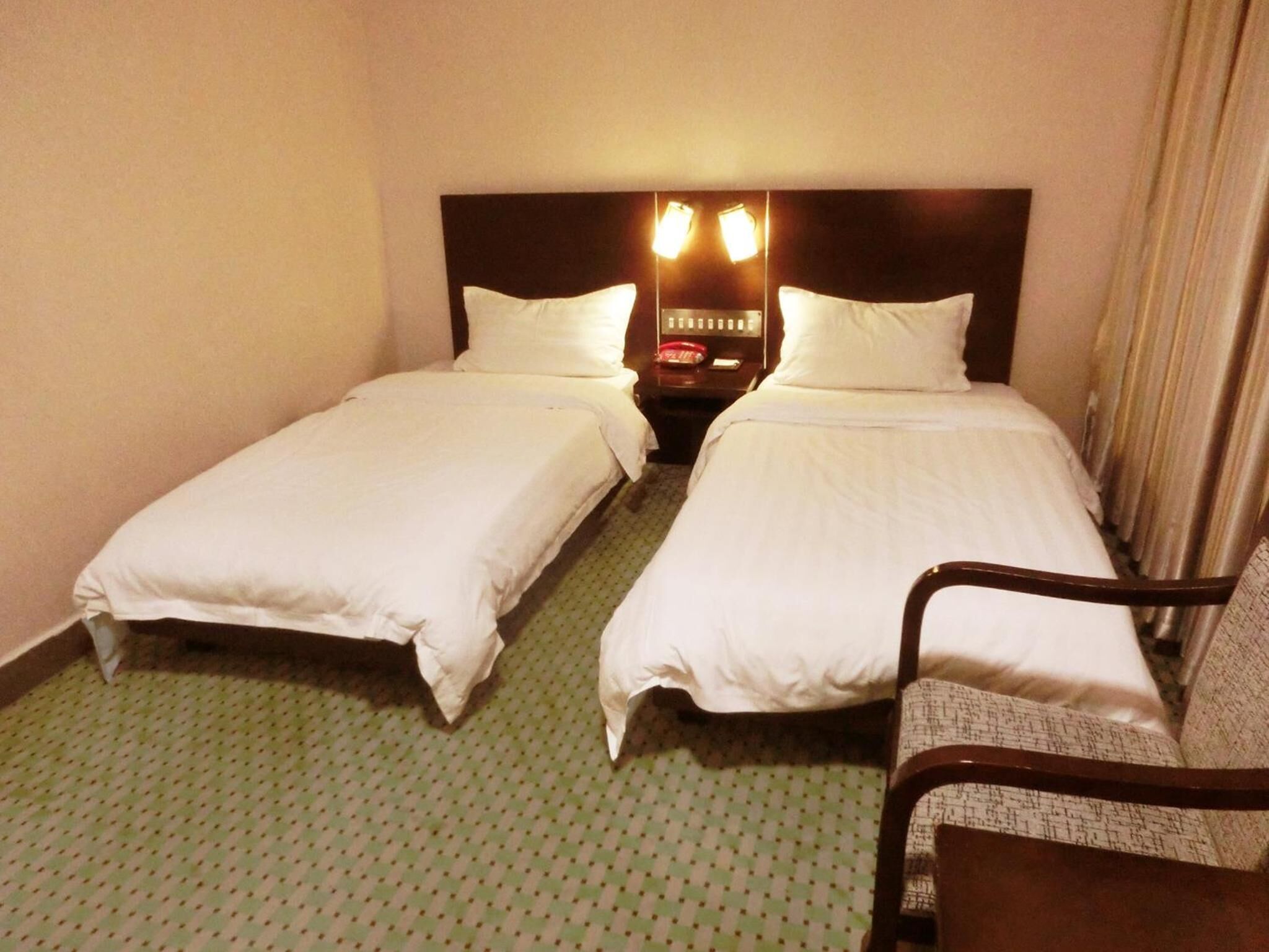 Una camera d'albergo con due letti singoli, un comodino con una lampada e una sedia.