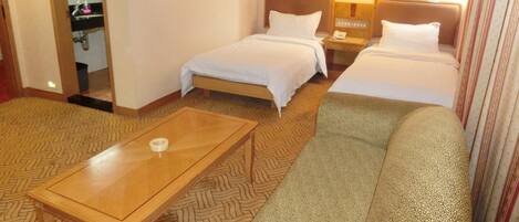 Habitación de hotel con dos camas individuales, un sofá, una mesa de madera y un baño visible a través de una puerta abierta.