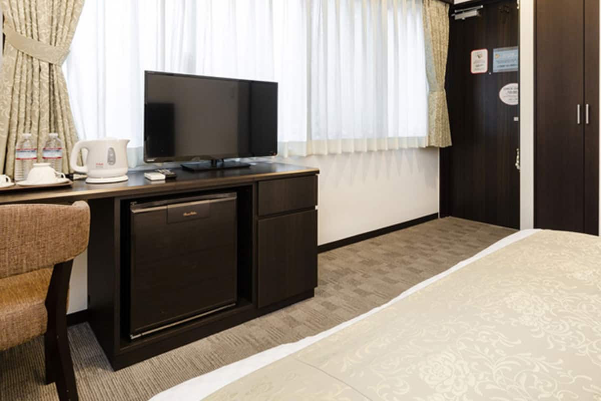 Una habitación de hotel con cama, escritorio con televisor, cafetera y armario.
