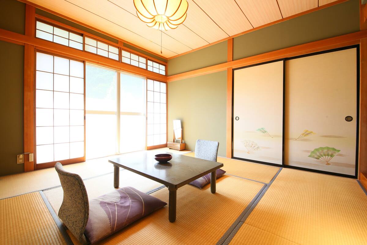 Ein traditioneller japanischer Raum mit Tatami-Bodenbelag, einem niedrigen Tisch, Kissen und verschiebbaren Türen.