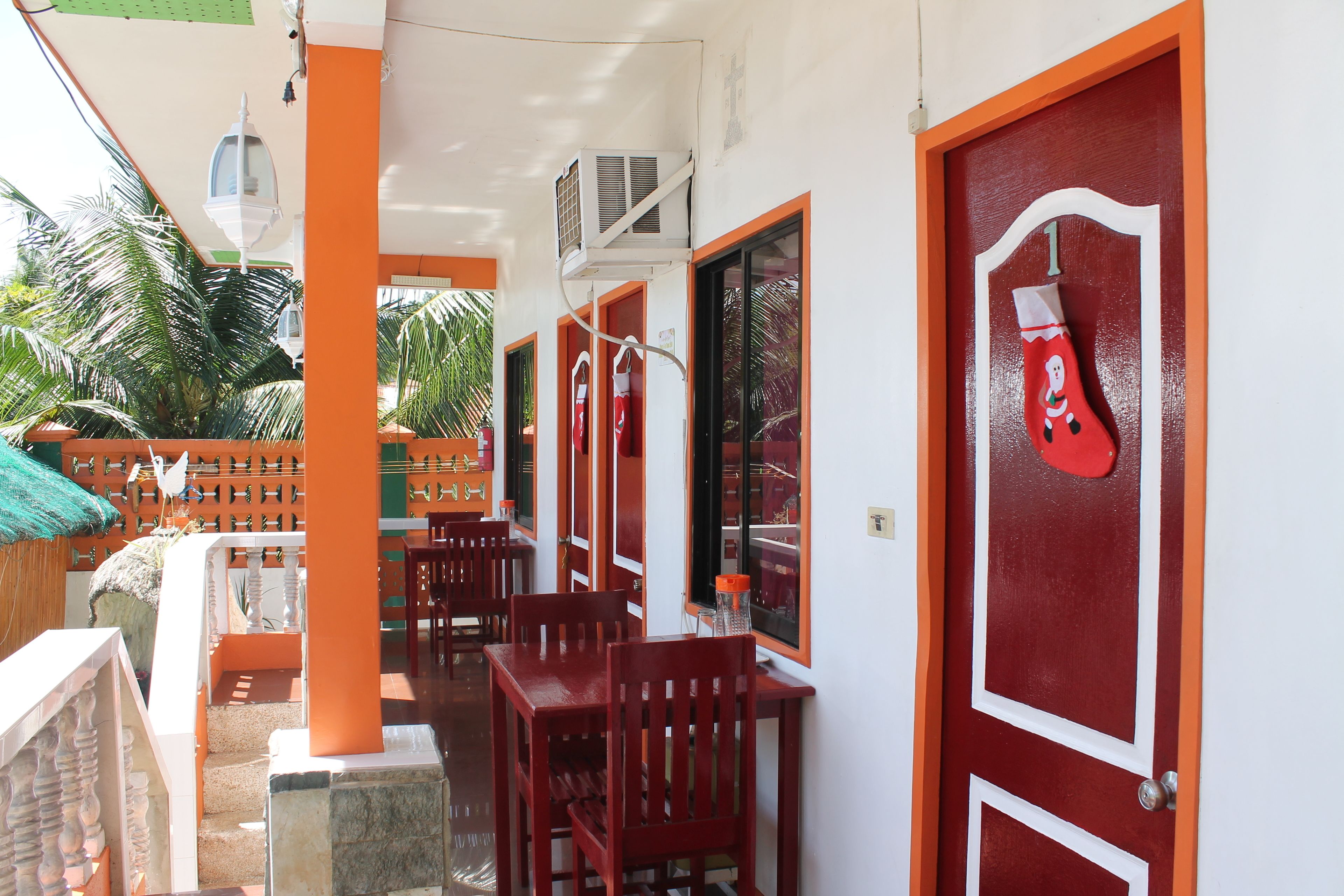 Un restaurant dont les portes sont encadrées de rouge, qui dispose de tables en terrasse et où l'on peut admirer une jolie décoration de Noël, notamment une grande chaussette de Noël.
