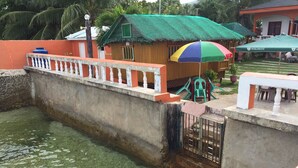 A small wooden structure with a thatched roof and a colorful umbrella, adjacent to a concrete water channel. - Maxvir Inn Beach Resort (Oslob)