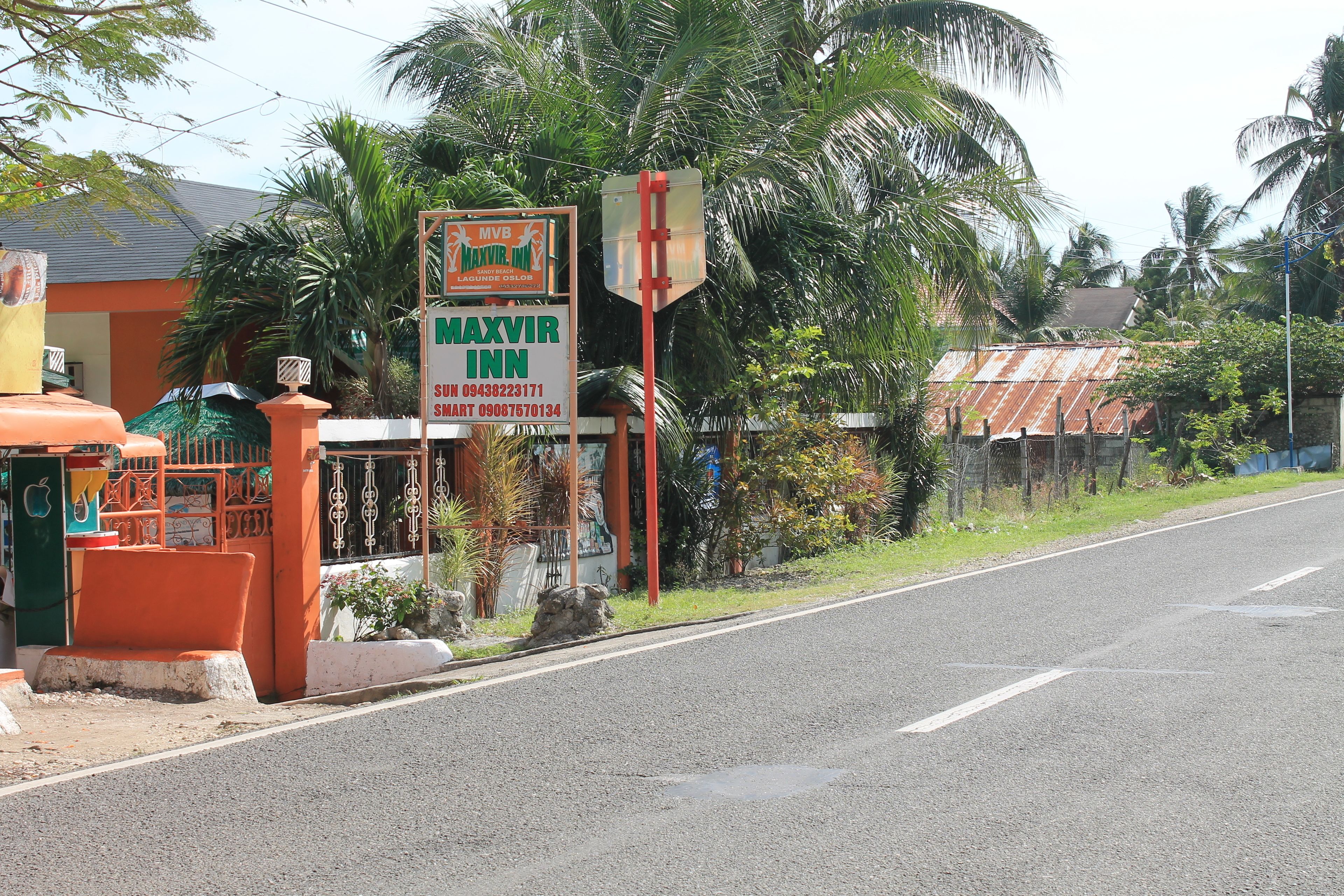 A MaxVir Inn signboard and a building with a red roof and palm trees.