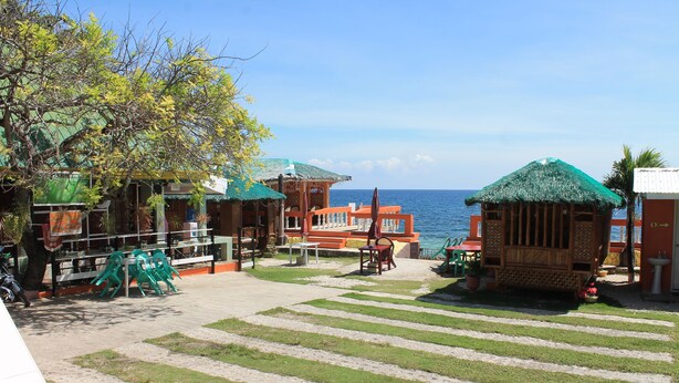 A beachfront area with thatched-roof structures, a paved walkway, and a view of the sea. - Maxvir Inn Beach Resort (Oslob)