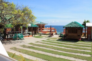 Zona de playa con estructuras de techo de paja, un paseo pavimentado y vista al mar.