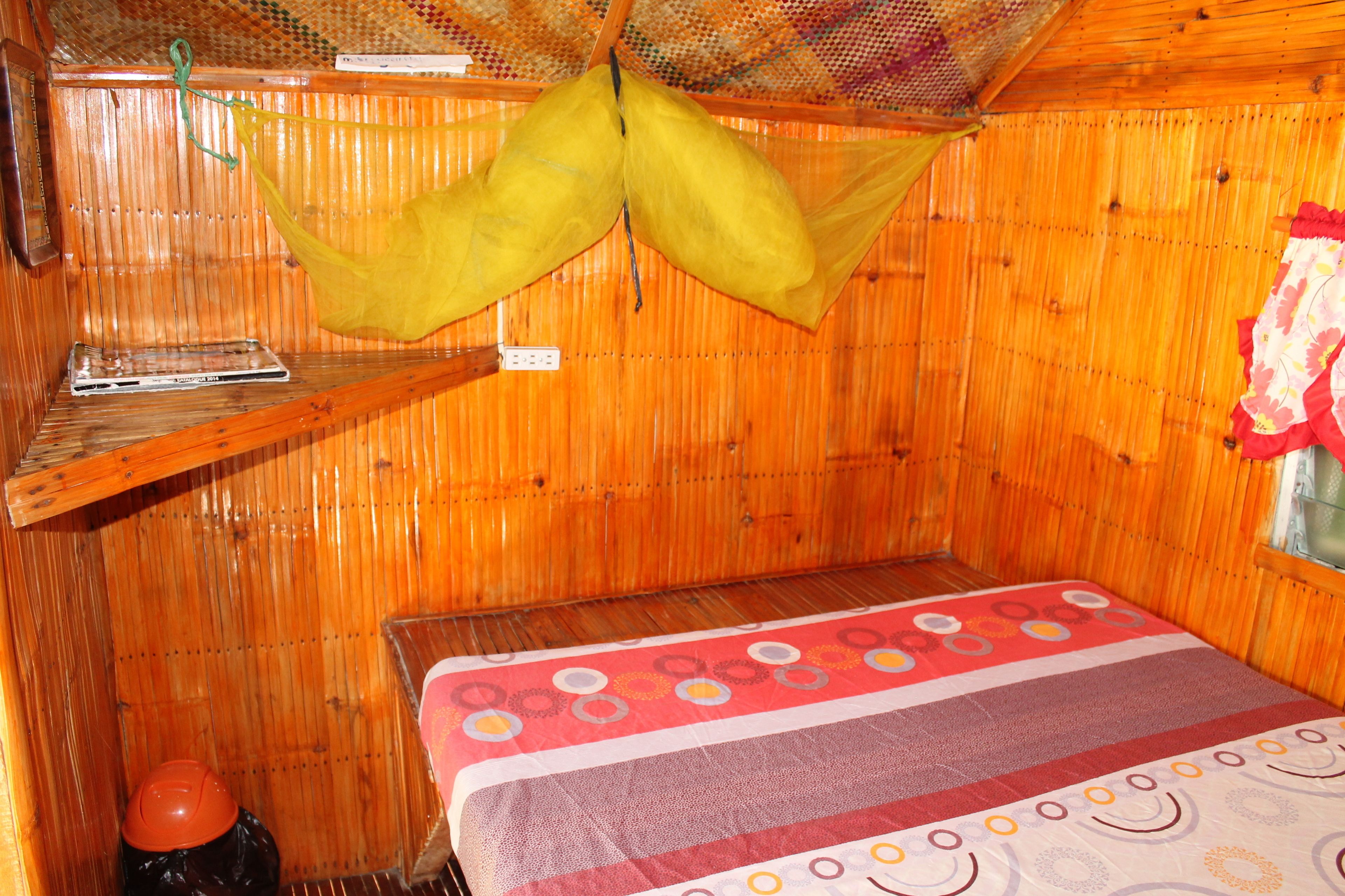 A small, wooden room with a bed, a shelf, and a hanging net.