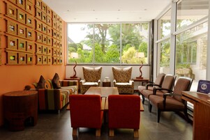 Un salón moderno con un ventanal grande, varias sillas, una mesa y una pared decorada con objetos enmarcados.