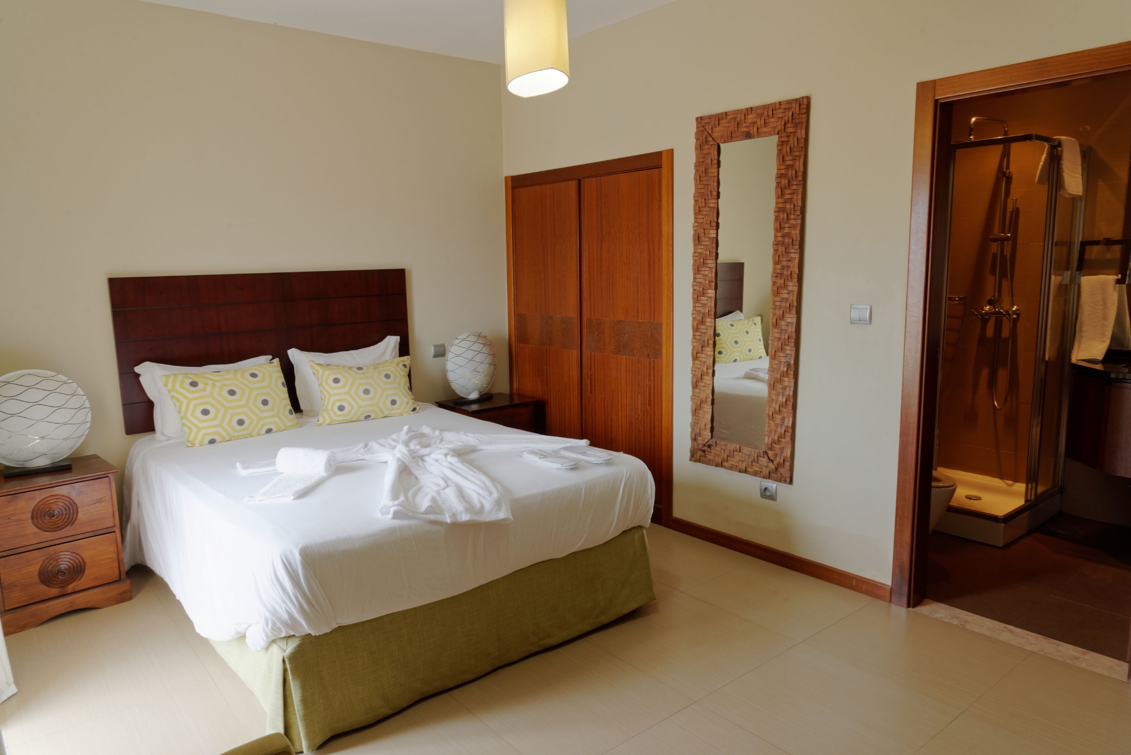 A hotel room with a bed, a nightstand, a mirror, and a shower area.