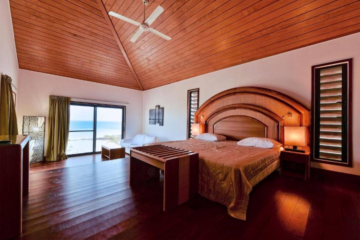 A spacious bedroom with a large bed, a ceiling fan, and a view of the ocean through a sliding door.