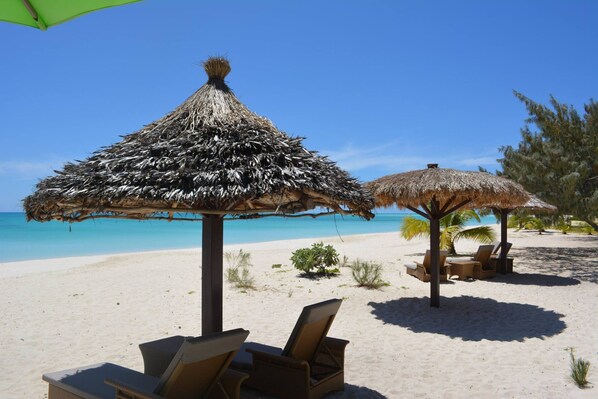 A beach with thatched umbrellas and lounge chairs.
