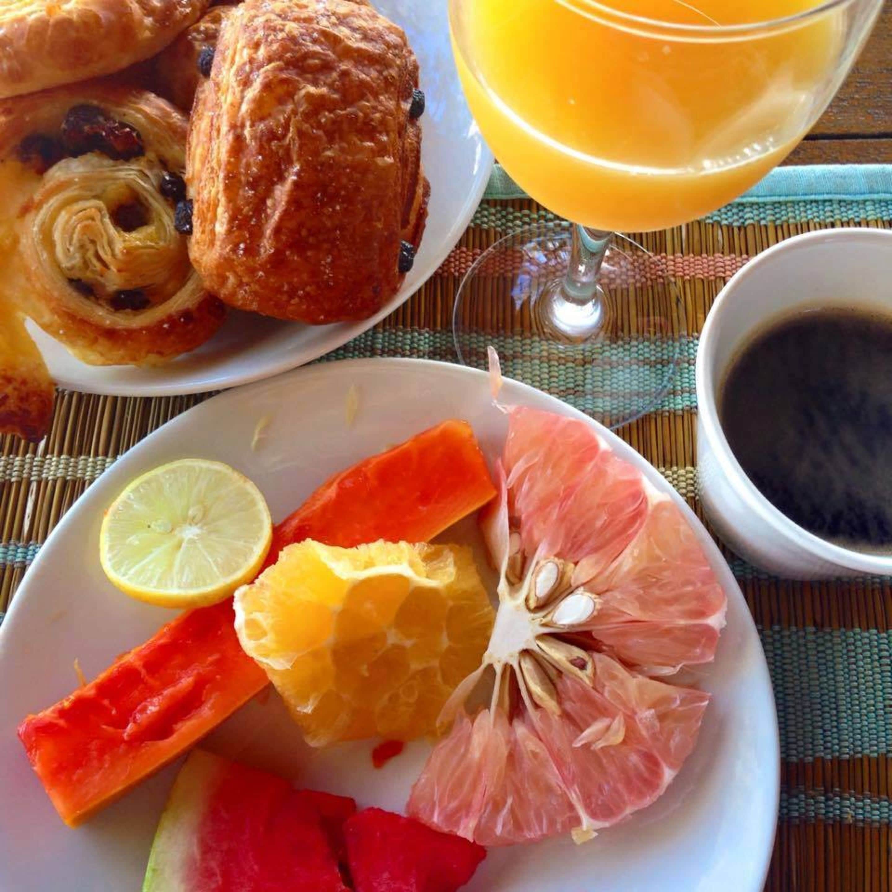 Un desayuno con pastelería, cítricos y un vaso de zumo de naranja.