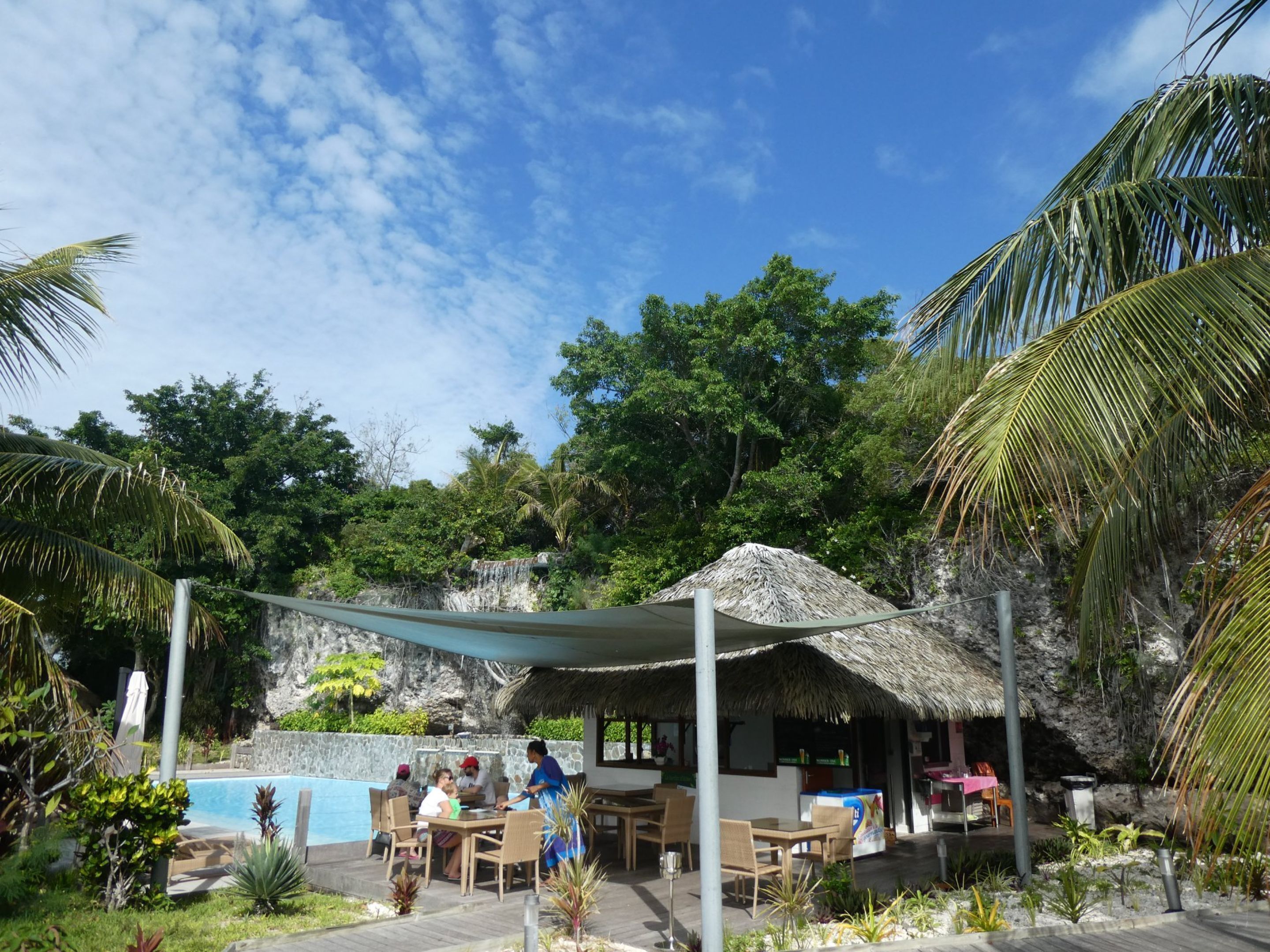 A poolside area with a thatched-roof structure, dining tables, and chairs.