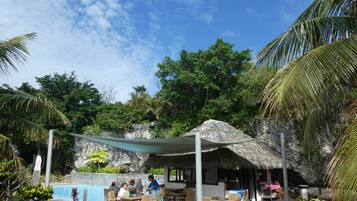A poolside area with a thatched-roof structure, dining tables, and chairs.