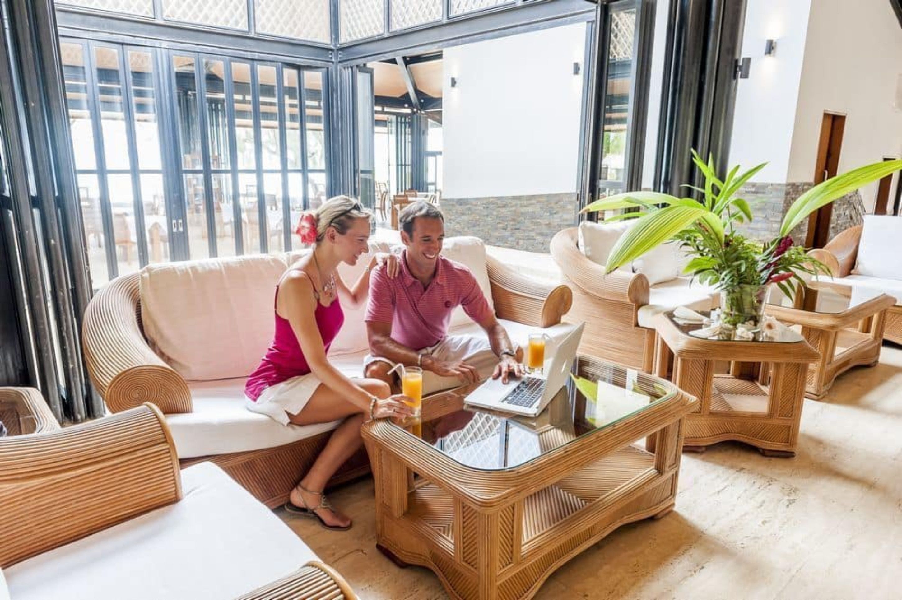 A modern lounge area with wicker furniture, a glass coffee table, and a view through large windows.