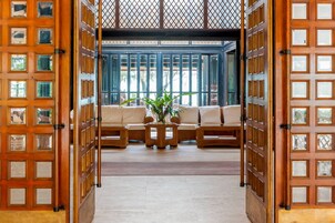 Un interior japonés tradicional con asientos de esteras de tatami, una mesa de madera central con una planta y vistas a través de una ventana con celosía.