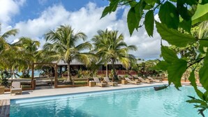 A poolside area with lounge chairs and palm trees, a building in the background, and a clear sky. - Paradis d' Ouvea (Ouvea)
