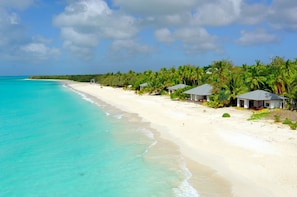 Uma praia com águas turquesa cristalinas, areia branca e vários edifícios pequenos com telhados vermelhos.