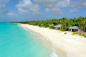 Una playa con aguas turquesas cristalinas, arena blanca y varios edificios pequeños con tejados rojos.