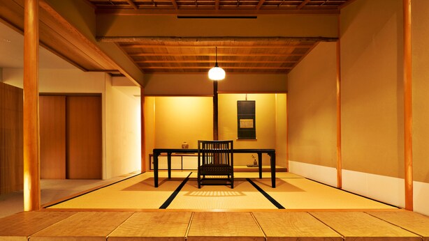 A traditional Japanese room with tatami flooring, a low wooden ceiling, and a central table with a chair. - Aoi Hotel Kyoto (Kyoto)