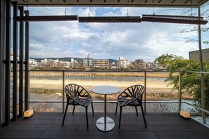 A balcony with two chairs and a table, overlooking a cityscape and a body of water.