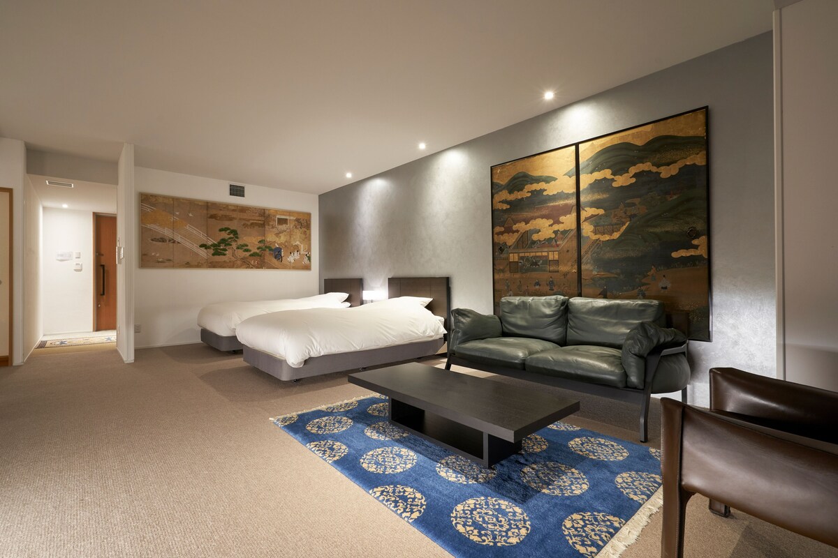 A modern hotel room with a bed, a sofa, a coffee table, and a large painting on the wall.