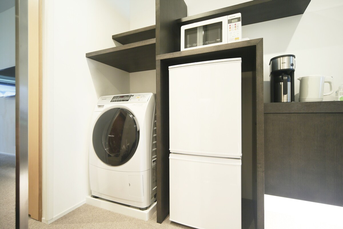 A compact kitchen with a washing machine, a refrigerator, and a coffee maker on the countertop.