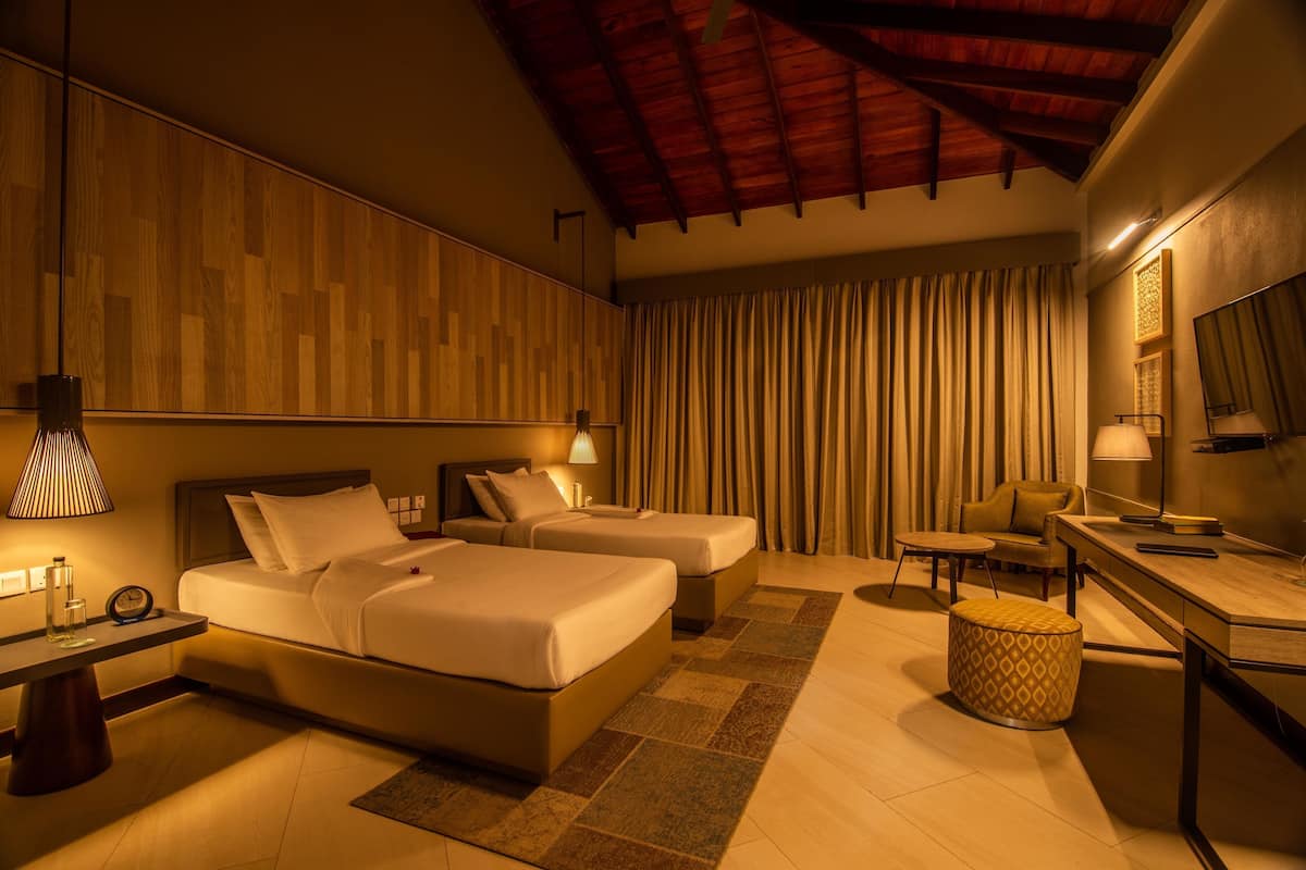 A hotel room with two beds, a desk, a chair, a lamp, and a mirror.