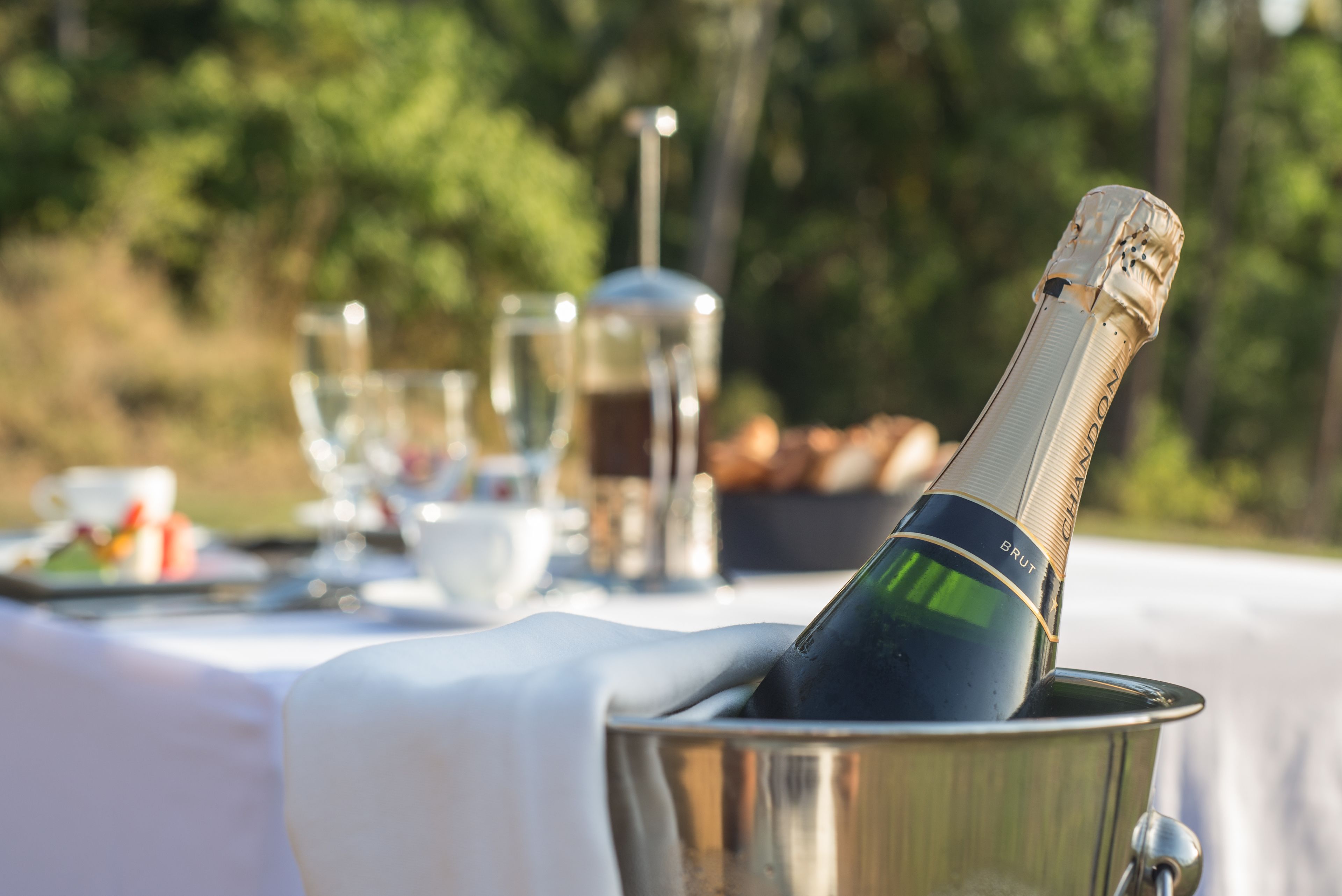 A bottle of champagne in a metal bucket on an outdoor table with a white tablecloth.