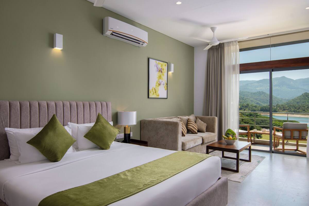 A hotel room with a large bed, a sofa, a dining table, and a view of the mountains.