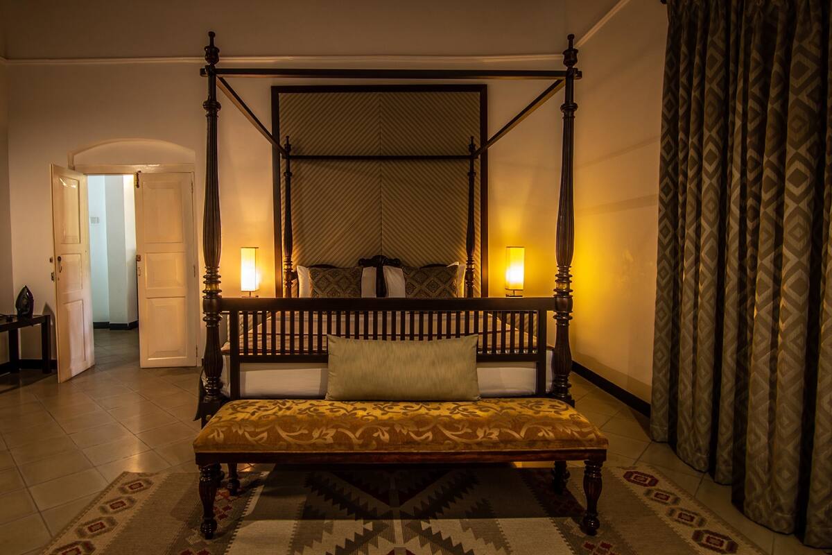 A four-poster bed with a headboard, two bedside lamps, and a patterned bedspread.