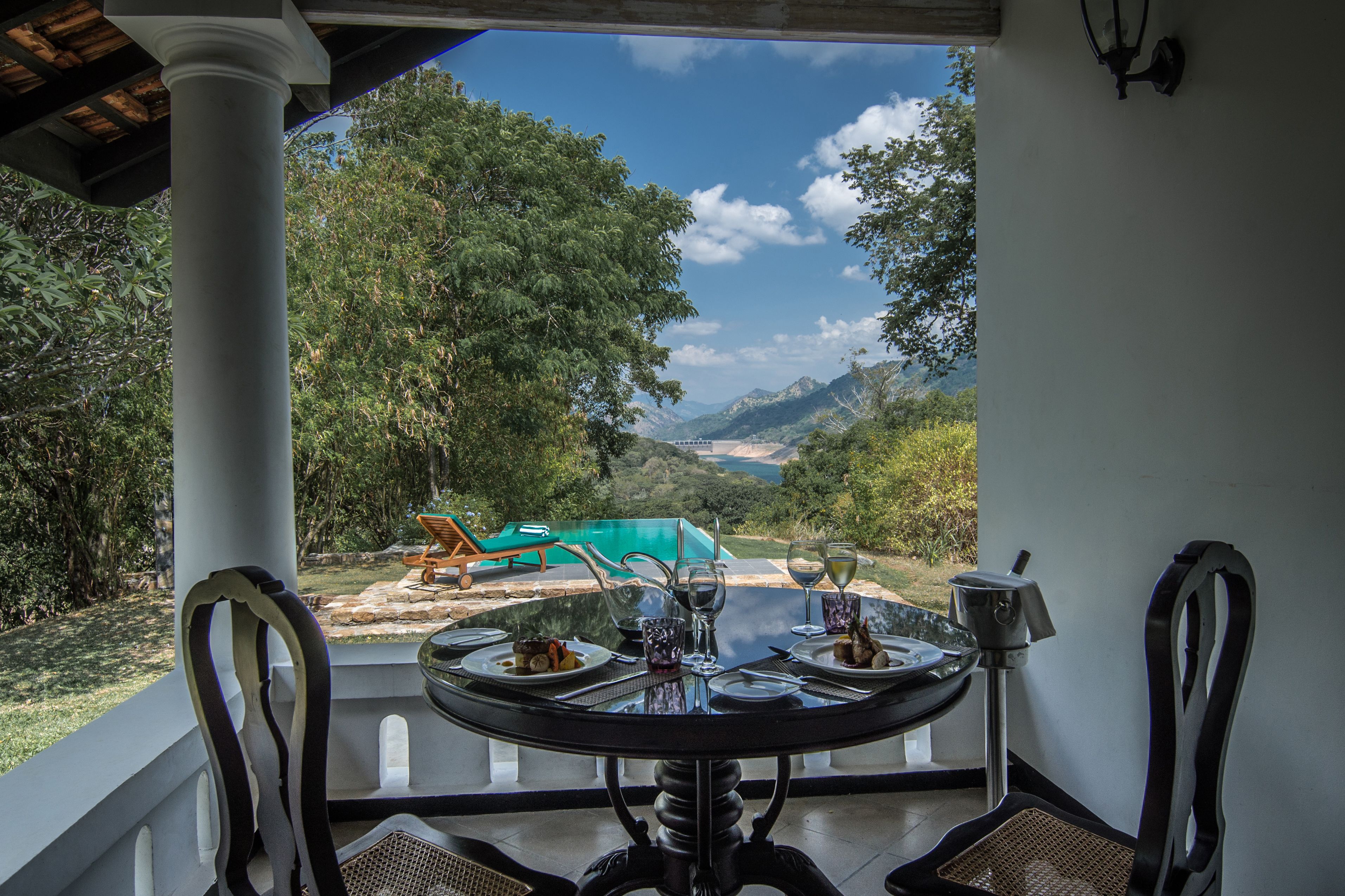 A dining table with chairs, a view of a swimming pool, and a mountainous landscape.