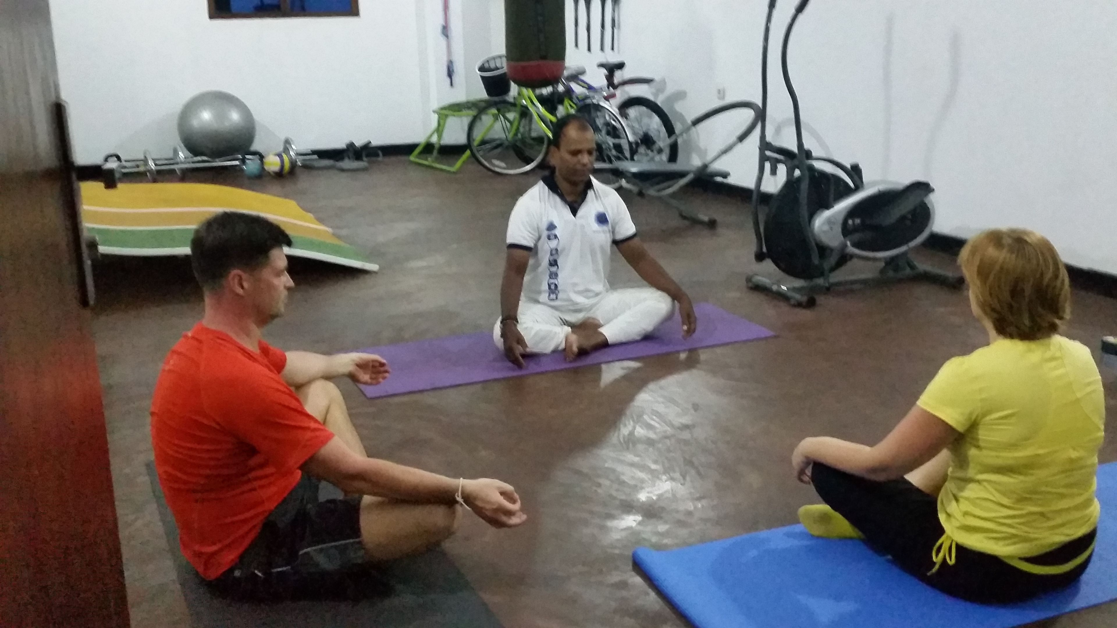 Een groep mensen zit op yogamatten in een ruimte met fitnessapparatuur.