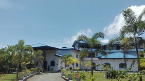 A large building with multiple levels and a blue roof, surrounded by lush greenery and palm trees. - Dhammika Magic Palace (Wadduwa)