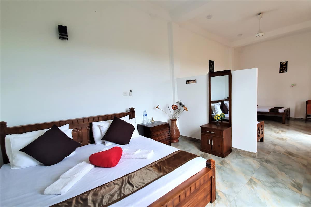 A hotel room with a bed, a wooden nightstand, a vase with flowers, a mirror, and a chair.