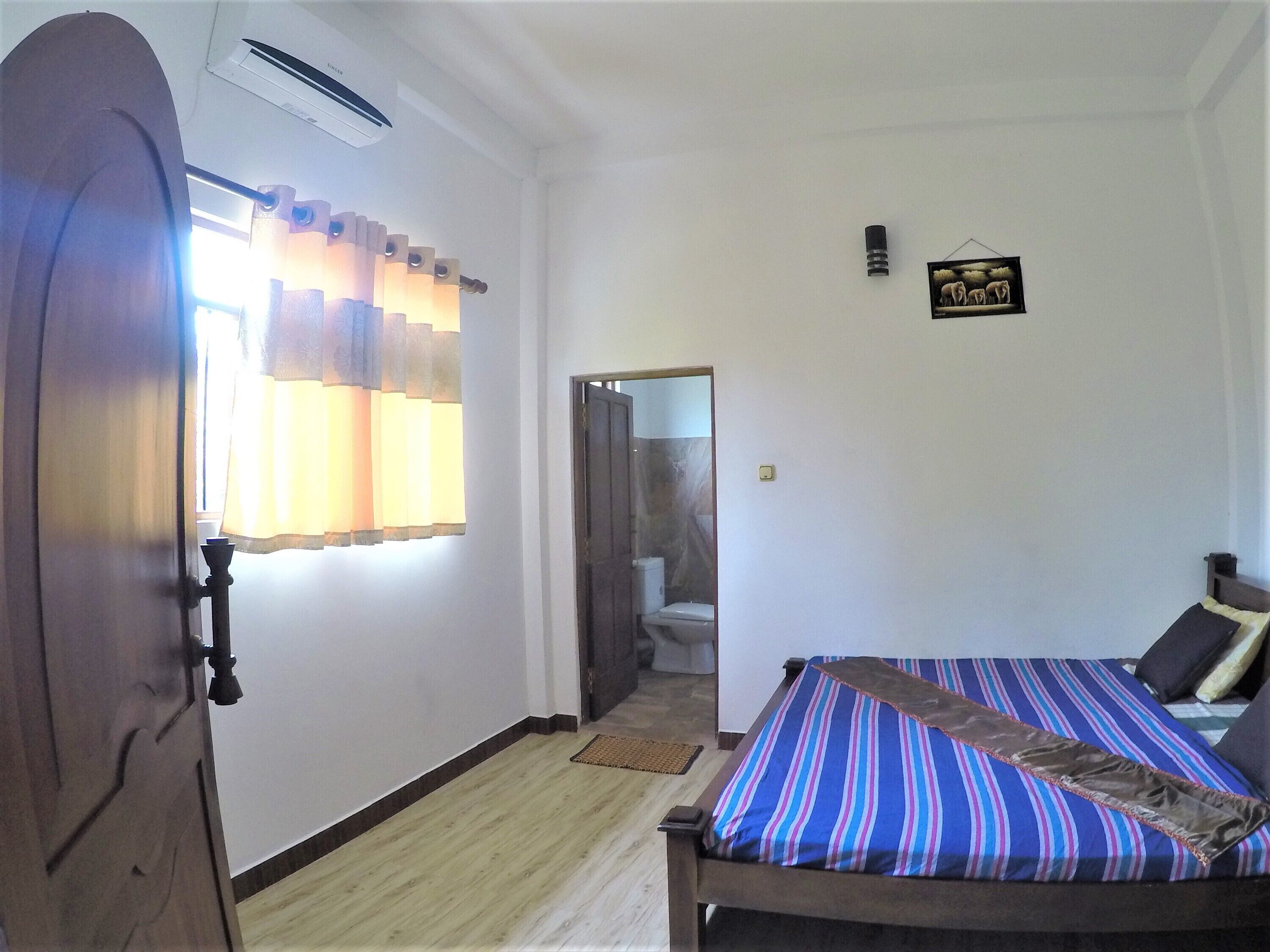 Una habitación con una cama, una puerta, un espejo y una lámpara fijada a la pared.