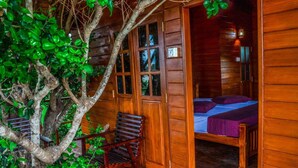A wooden cabin with a bed, a chair, and a tree in the foreground. - Lake Villa Resort (Weerawila)
