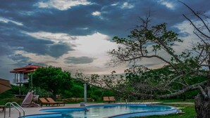 A swimming pool with a curved edge, surrounded by grass and trees. - Lake Villa Resort (Weerawila)