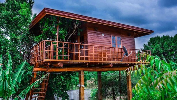 A wooden cabin with a balcony, surrounded by lush greenery. - Lake Villa Resort (Weerawila)