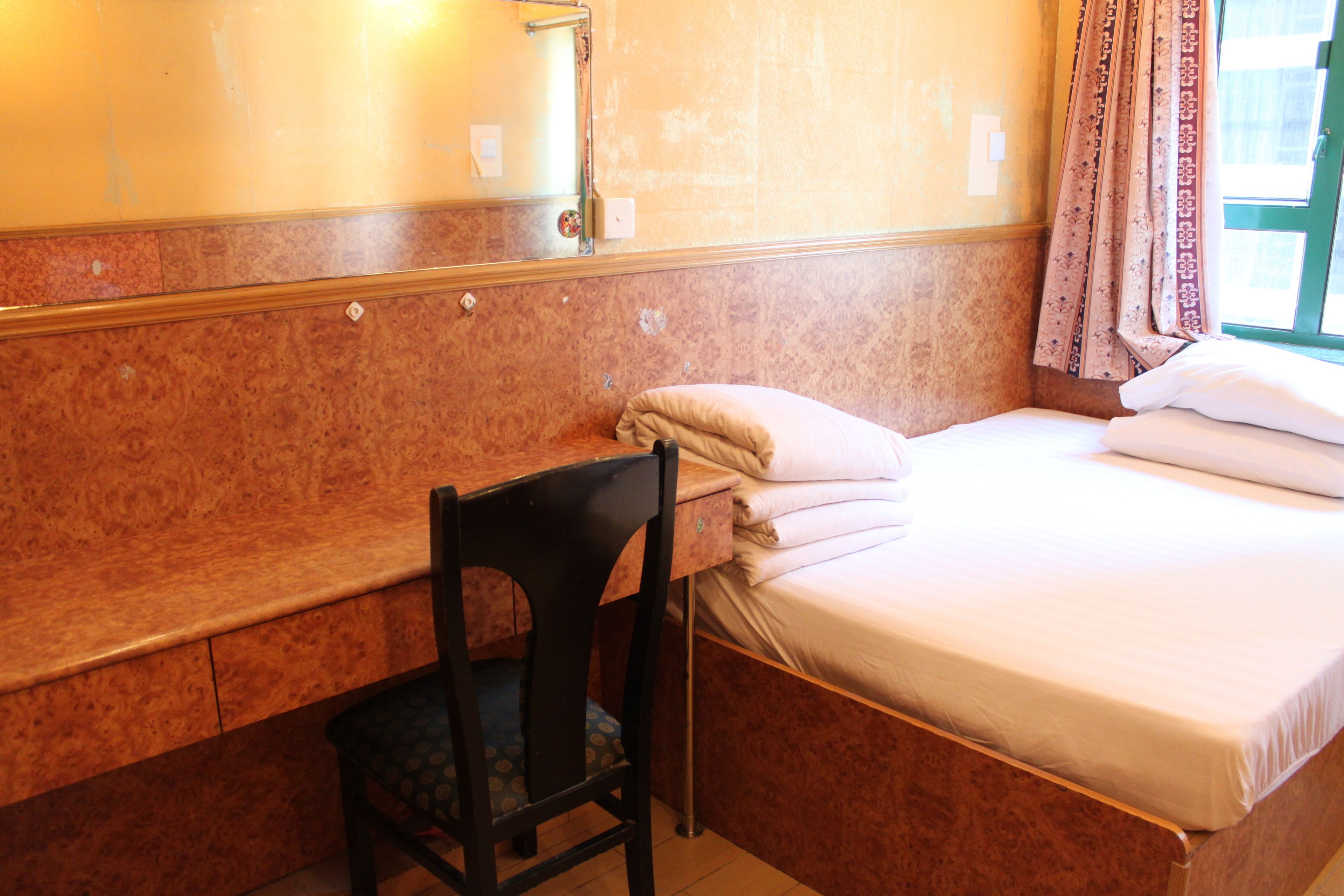 A small room with a bed, a chair, a desk, and a mirror.