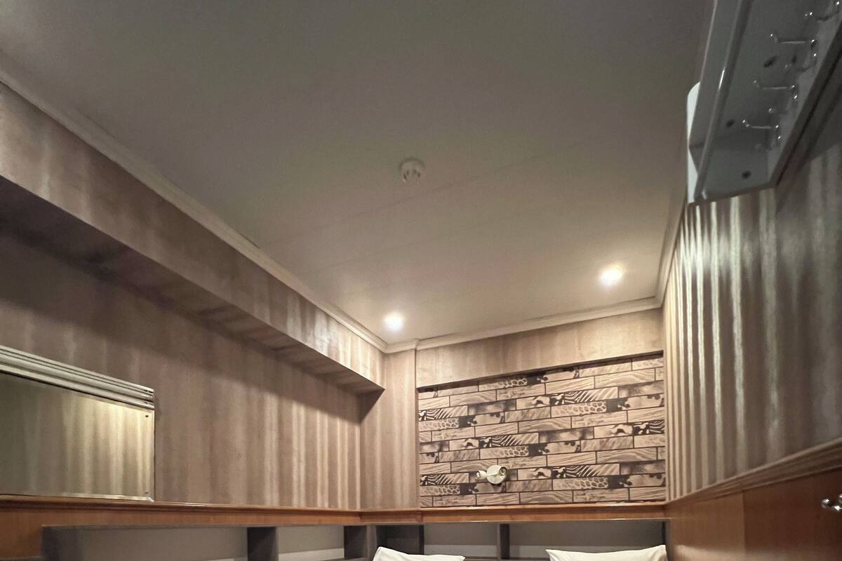 A hotel room with two single beds, a wooden floor, a wall with a patterned design, and a ceiling light.