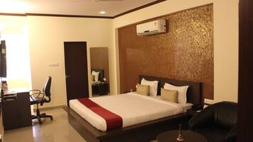 A hotel room with a large bed, a desk with a chair, a small round table, and a ceiling fan.