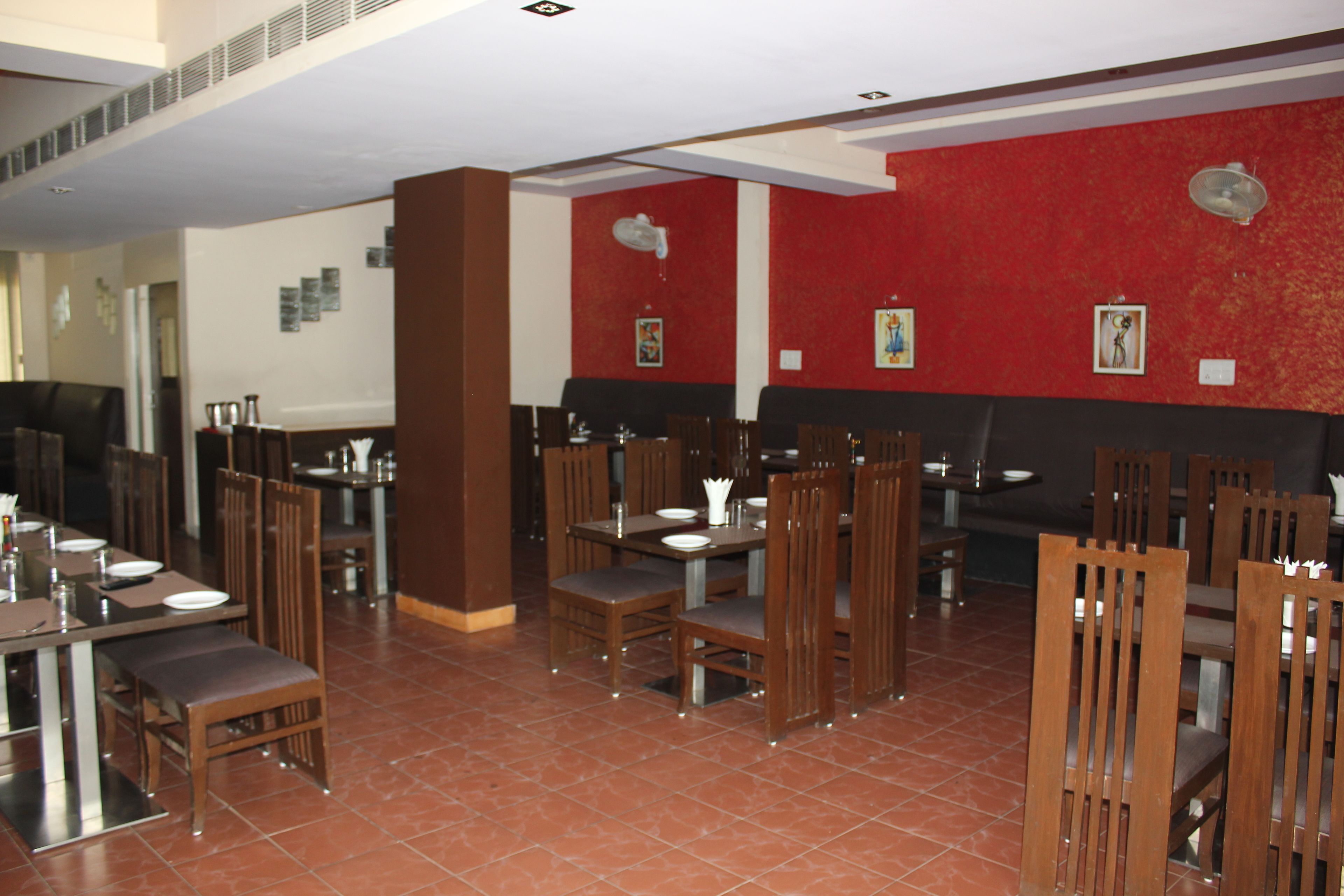 A restaurant with multiple tables and chairs, red and black walls, and tiled flooring.
