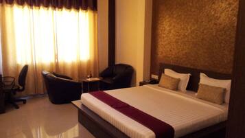 A hotel room with a large bed, a desk, a chair, and a window with curtains.
