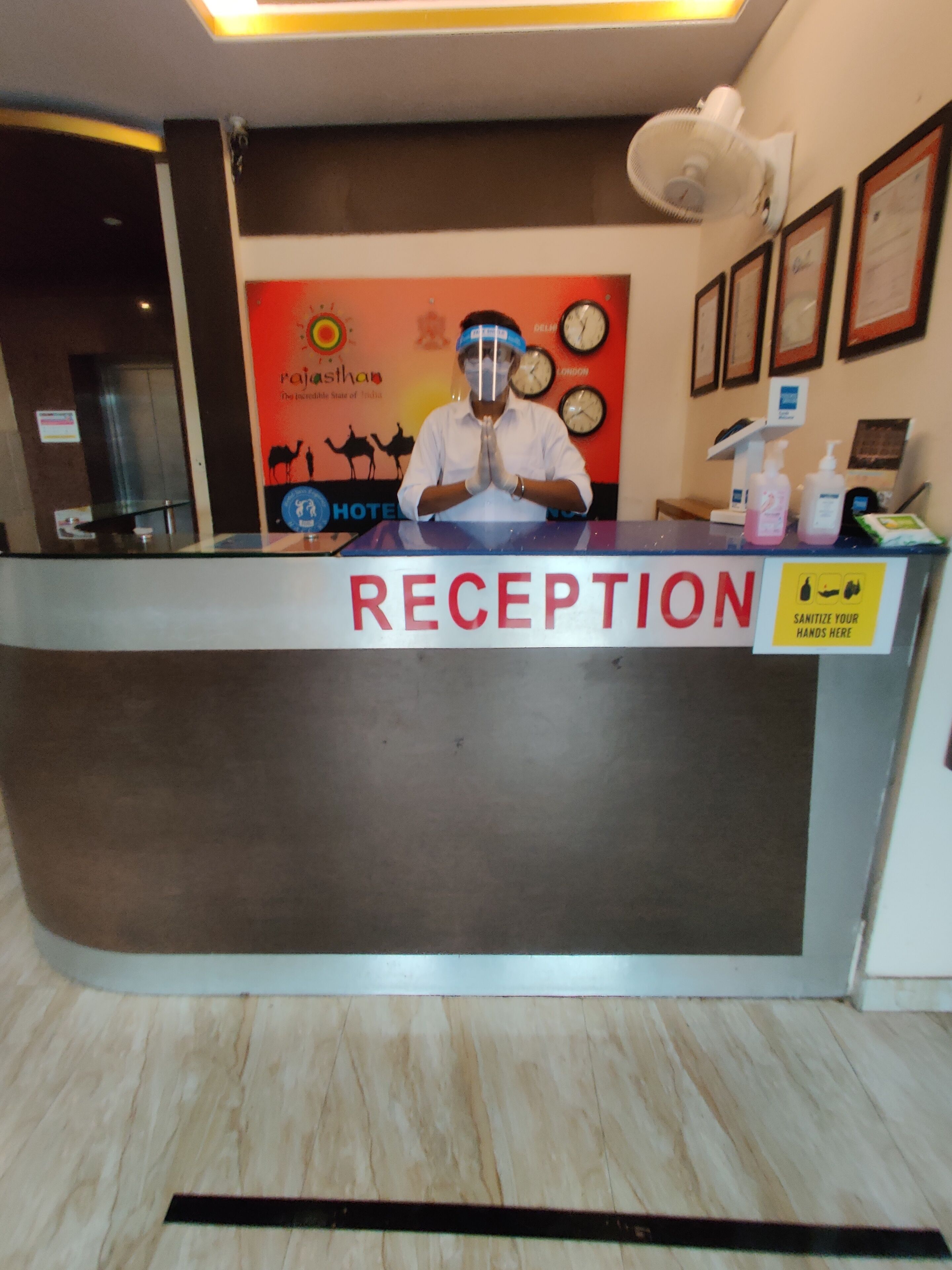 Un comptoir d’accueil avec une pancarte indiquant « RÉCEPTION » et une autre pancarte indiquant « VEUILLEZ DÉSINFECTER VOS MAINS ICI ».