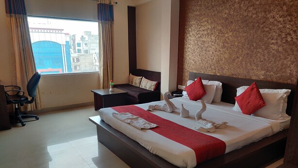 A hotel room with a large bed, a desk, a chair, and a view of buildings through the window. - Hotel Savi Regency (Jaipur)