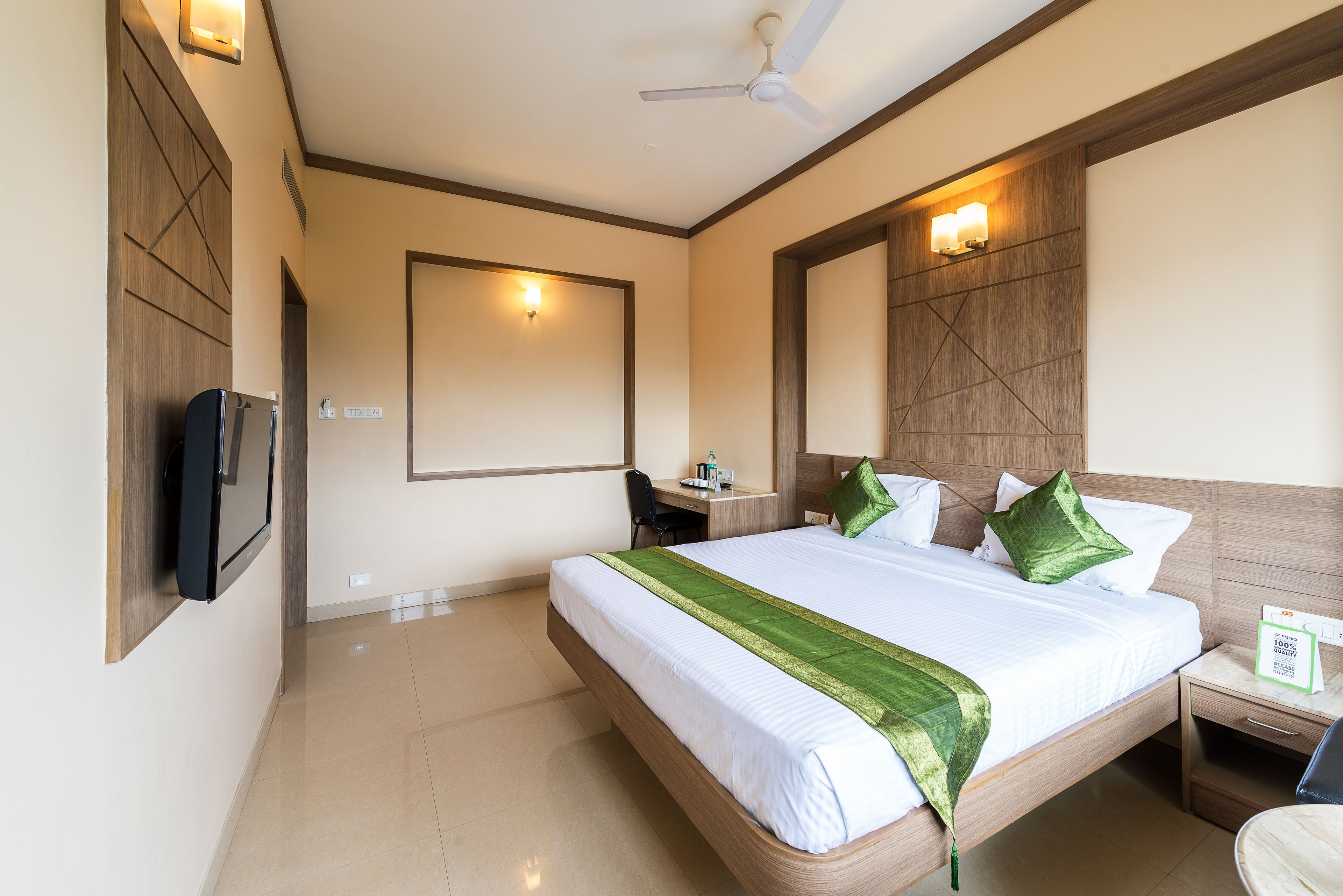 A hotel room with a large bed, a desk, a chair, a television, and a ceiling fan.